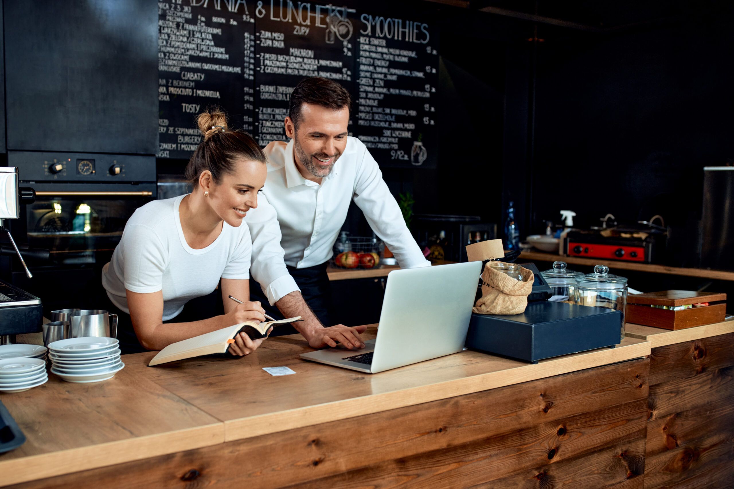 deux employés dans un restaurant qui sourient devant un ordinateur.